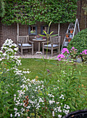 Cozy seating area under an overgrown wall with flowering plants in the foreground