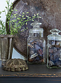 Decorative arrangement with glass jars and metal vase on a dark table