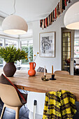 Esstisch mit heller Holzplatte, buntem Wollplaid und modernen Pendelleuchten