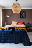 Schlafzimmer mit Rattan-Pendelleuchte und Katze liegt auf dunkelblauer Bettdecke