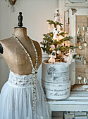 Old dressmaker's dummy with pearl necklace and lace-trimmed garment, behind it a Christmas tree decorated with cotton dolls