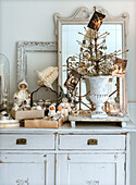 Kahler Weihnachtsbaum mit Weihnachtsschmuck und alten Karten in einer Urne, daneben Baumwollpuppen