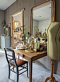 Wooden table with antique decorative objects and large mirror, with a dressmaker's dummy next to it