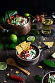 Vegan chili served with plant-based sour cream, chili pepper, coriander and tortilla chips