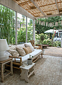 Covered terrace with bamboo sofa, throw pillows and plants in the background