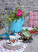 Sommerlicher Gartentisch mit Blumen in blauer Teekanne und Teeservice