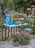 Blau gestrichener Gartentisch mit Blumenarrangement und alten Teekannen