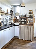 Small kitchen with tiled backsplash and wooden floor, white kitchen cabinets and an under-cupboard curtain