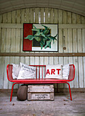 Red metal bench with decorative cushions in front of a wooden wall in the garden shed