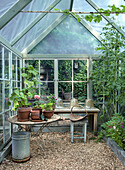 Greenhouse with potted plants, garden table and stool on gravel floor