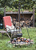 Fire pit with hanging kettle and garden chair in front of wood pile in the garden