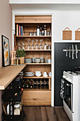 Open wooden kitchen shelves with crockery and wine glasses, next to gas cooker