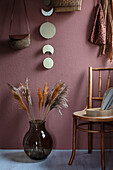 Dried pampas grasses in a vase next to a wooden chair in front of a wall in dusky pink