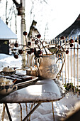 Winterlicher Gartentisch mit Keramikvase und Gebäck im Schnee