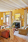 Old-fashioned living room with yellow-painted walls, fireplace and fabric curtains with a floral pattern