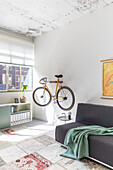 Bicycle on wall bracket, dark sofa and patterned carpet in light-colored room