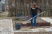 Frau bei Anlegen eines Gemüsebeets mit Flechtwand aus Weidenzweigen und Weg anlegen mit Kies