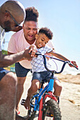 Happy gay male couple helping son ride a bike