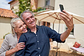 Senior couple taking selfie outside sunny villa