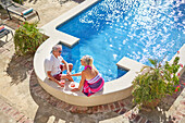 Senior couple drinking cocktails by swimming pool