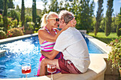 Senior couple hugging and kissing by swimming pool