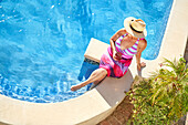 Senior woman drinking cocktail at sunny poolside
