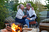 Senior couple drinking wine and hugging by fire pit