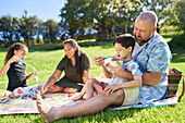 Father feeding son with Down syndrome on picnic blanket