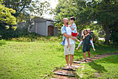 Parents carrying daughter and son on path in sunny backyard