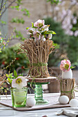 Lenz rose blossoms (Helleborus Orientalis) in vases and between fine stem Chinese reed 'Gracillimus', Easter eggs as table decoration