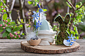 Blaustern (Scilla Siberica), Federn, Eierschale und Osterhase als Osterdeko auf Gartentisch