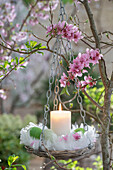 Blumenampel mit Osternest aus Federn, Eiern und Kerze und Blütenzweigen der Zierkirsche