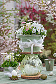 Tiered flower pot made of horned violets, daisies and glass vase, Easter eggs in small moss nests with feathers and on table