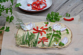 Osterfladen, roher Teig dekoriert mit frischen Kräutern, Zwiebelstreifen und Blüte aus Paprikastreifen auf Holzbrett, vor dem Backen