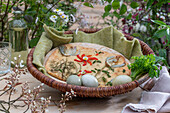 Easter flat bread decorated with herbs, fried onions and blossom of pepper strips, Easter eggs and bouquet of daisies in wicker basket