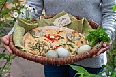 Easter cake decorated with herbs, fried onions and a blossom of pepper strips, Easter eggs and a bouquet of daisies in a wicker basket with an Easter greeting