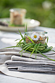 Cloth napkins, table decoration, glass with daisies (Bellis perennis), wrapped with blades of grass