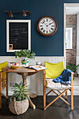 Cosy dining area with wooden folding table and yellow director's chairs in front of dark blue wall