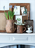 Snowdrops (Galanthus nivalis) and grape hyacinths (Muscari) in rustic vases on a mantelpiece