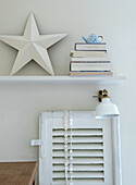 Decorative shelf with star, books and teapot above a wall lamp