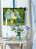 Side table with candle holder, vase with forget-me-nots and flower painting