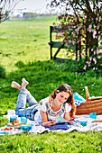 Junge Frau liest Zeitschrift auf Picknickdecke im Freien
