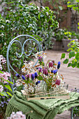 Felsenbirne (Amelanchier), Schachbrettblume (Fritillaria meleagris), Traubenhyazinthen (Muscari) und Taubnessel, einzelne Blüten in Vasen auf der Terrasse