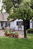 Gepflasterter Innenhof mit Gartentisch und Topfpflanzen vor reetgedecktem Haus