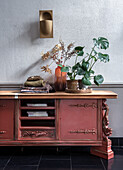 Red vintage sideboard with plants and dried flower arrangement in front of textured wall