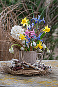 Spring bouquet of hyacinths, dwarf iris 'Clairette', snowdrops, grape hyacinths 'White Magic' in coffee cup, pussy willow and straw nest
