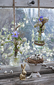 Traubenhyazinthe 'Withe Magic' (Muscari) und Windröschen (Anemone blanda) in hängenden Blumenvasen vor Fenster und Osterhasenfigur