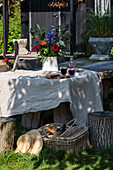 Rustic garden table with linen tablecloth and flower vase, surrounded by tree stump stools