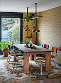 Dining room with solid wooden table, colourful chairs, hanging copper lights and yellow wallpapered wall