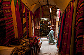 Morocco,Looking past clothes for sale in narrow passageway to man walking down alley,Fez